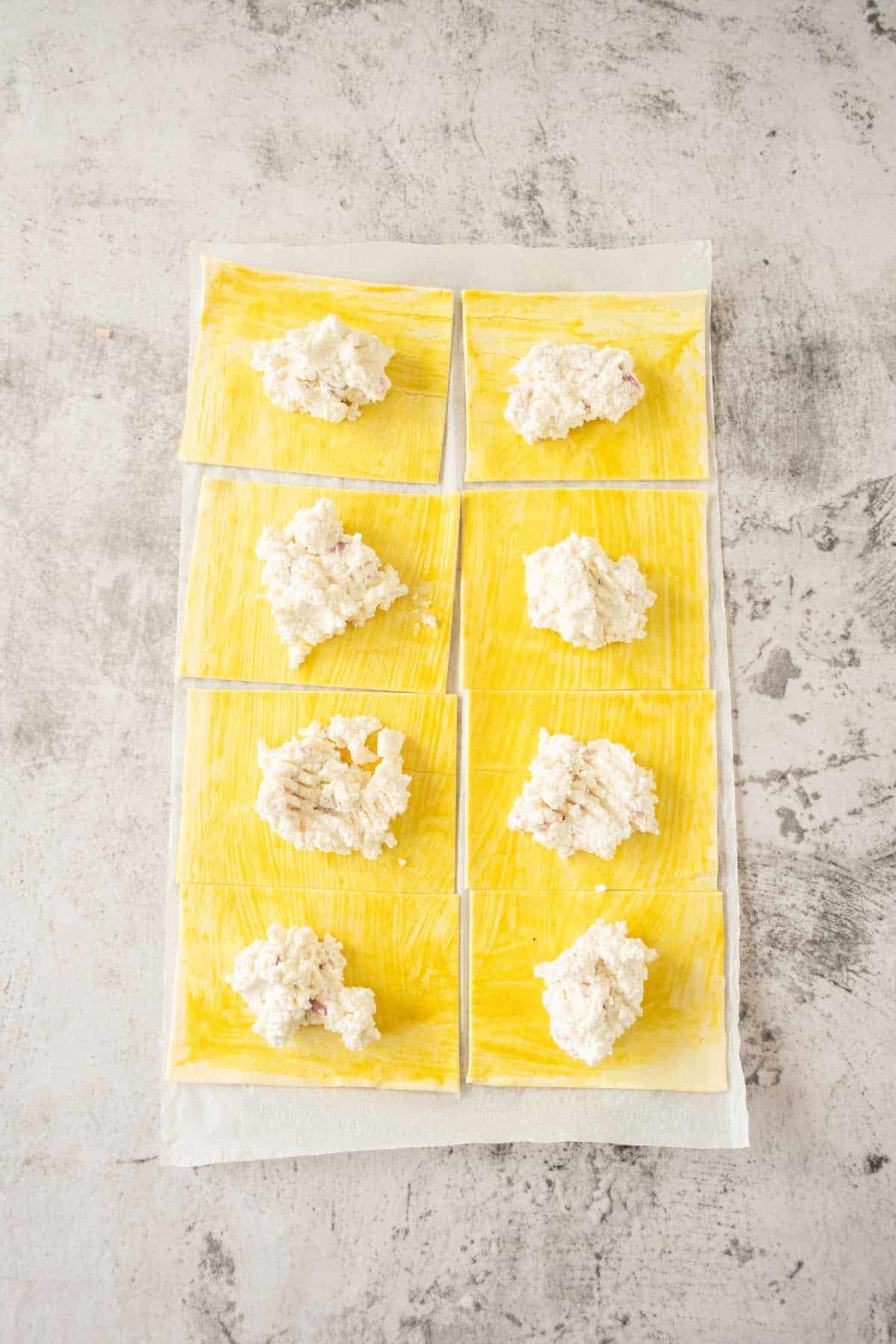 Fresh puff pastry sheets with dollops of ricotta cheese on a kitchen surface.