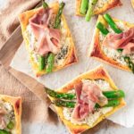 Freshly baked ricotta, asparagus and prosciutto tartlets on a serving surface.