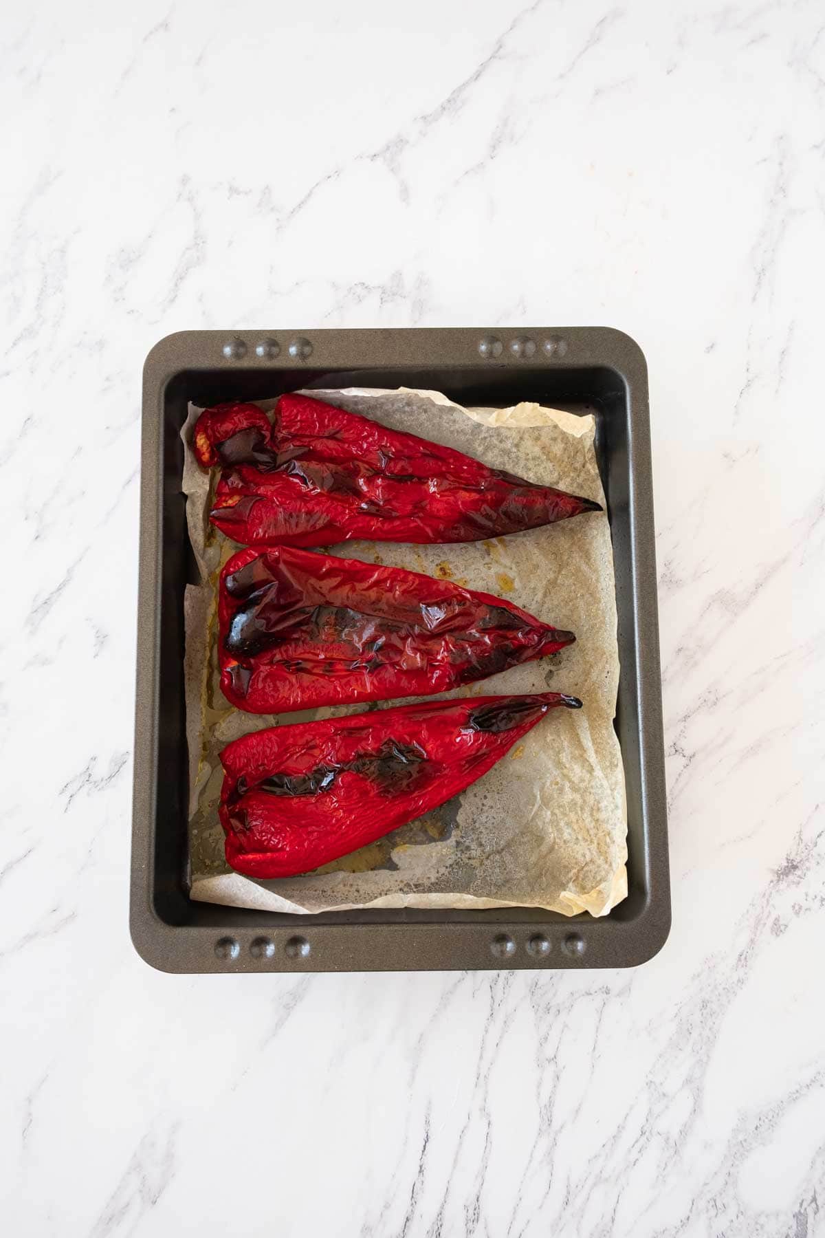 Roasted red peppers, slightly blackened in a roasting pan.