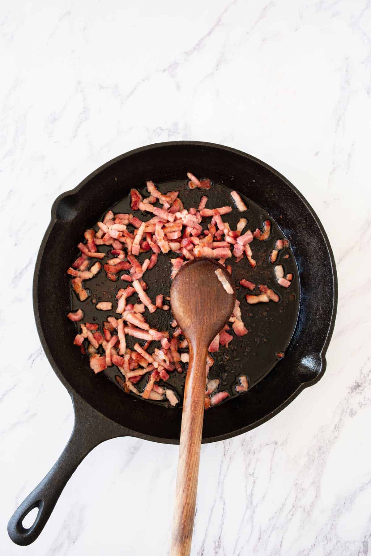 Stirring bacon bits in a cast iron pan with a wooden spoon.