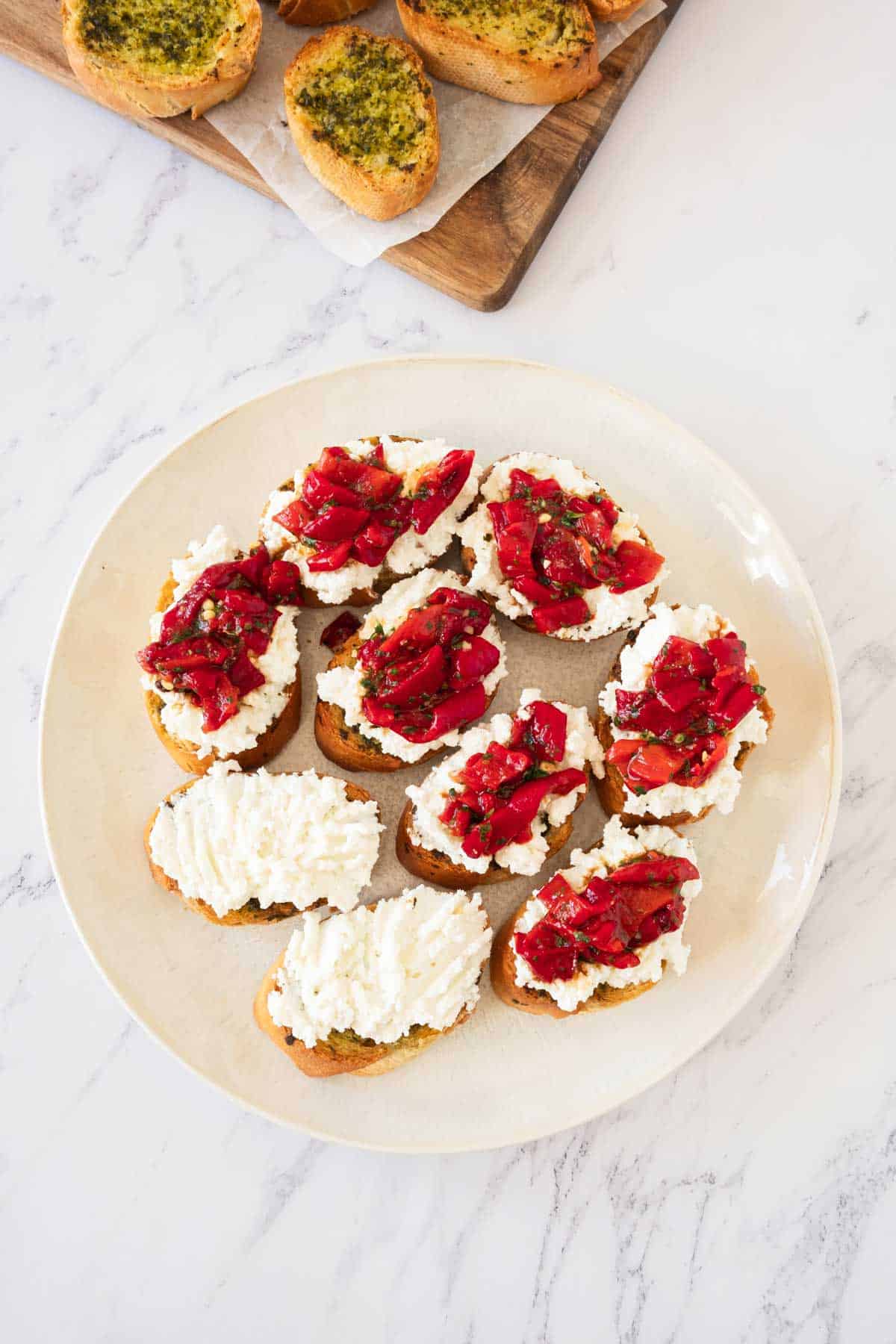 A plate of bruschetta with ricotta topped with roasted red peppers.
