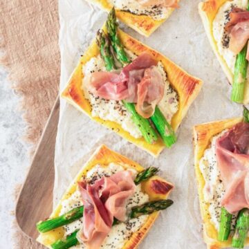Freshly baked asparagus and prosciutto tartlets on parchment paper.