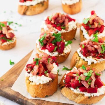 Slices of roasted red pepper bruschetta with ricotta on a wooden board.
