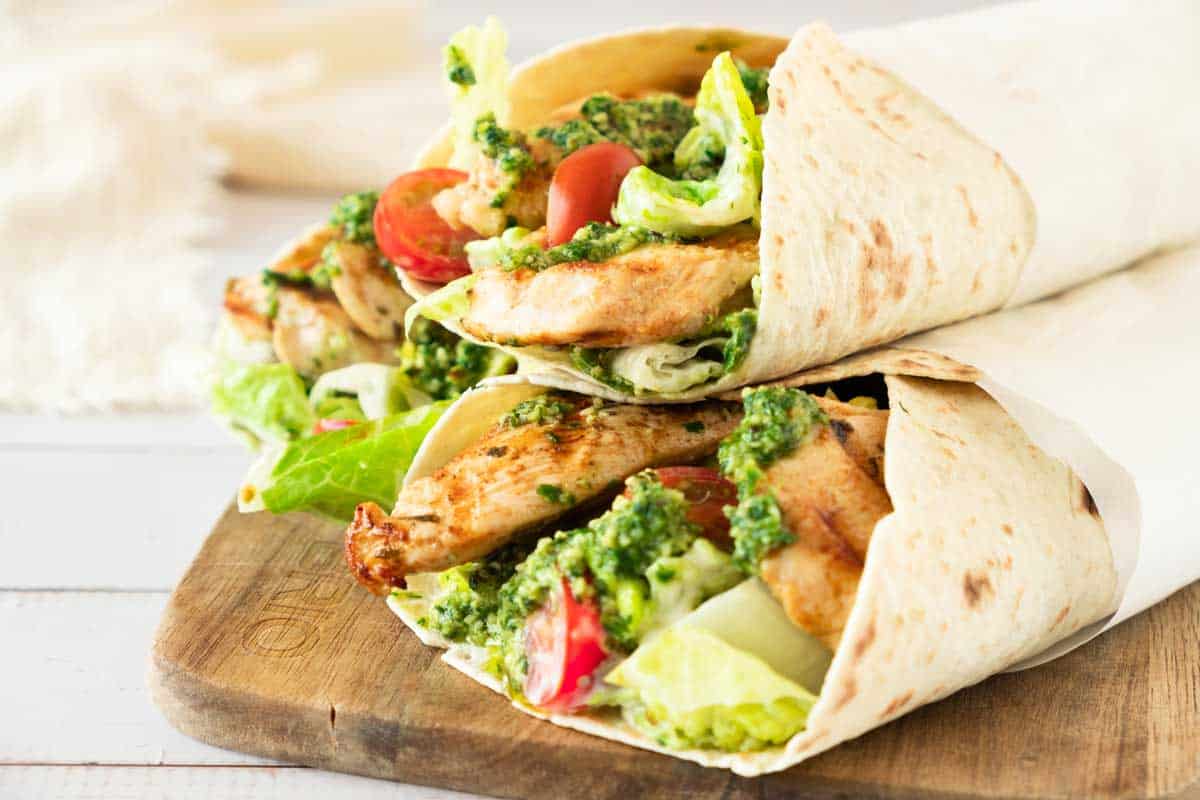 Grilled chicken wraps with pesto sauce, served on a wooden cutting board.