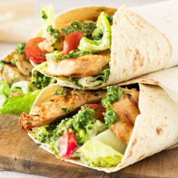 Chicken and vegetable wraps with pesto on a wooden board.