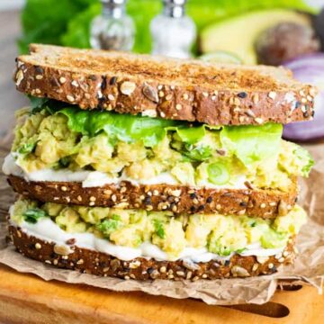 A stack of vegan chickpea and avocado sandwiches on a wooden board.