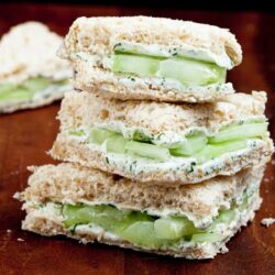 A stack of cucumber sandwiches with cream cheese and herbs on whole grain bread, crusts removed.
