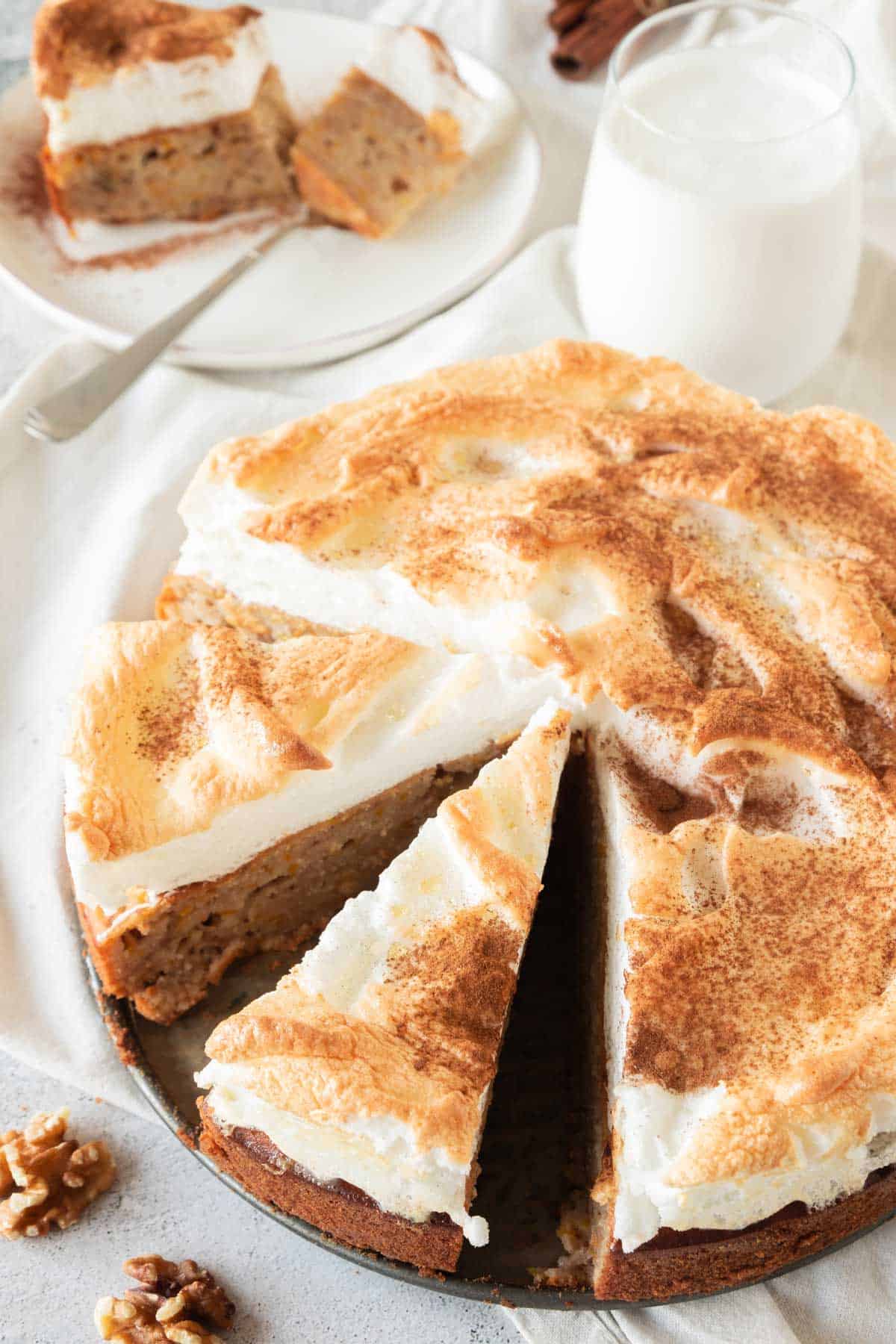A pumpkin spiced coffee cake with one slice removed, topped with toasted meringue, served with a glass of milk on a light background.