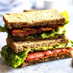 A vegan blt tempeh sandwich with crisp lettuce and tomato slices between toasted whole wheat bread slices.