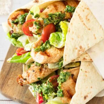 Grilled chicken wraps with fresh vegetables and green sauce in folded flatbreads, served on a wooden cutting board.