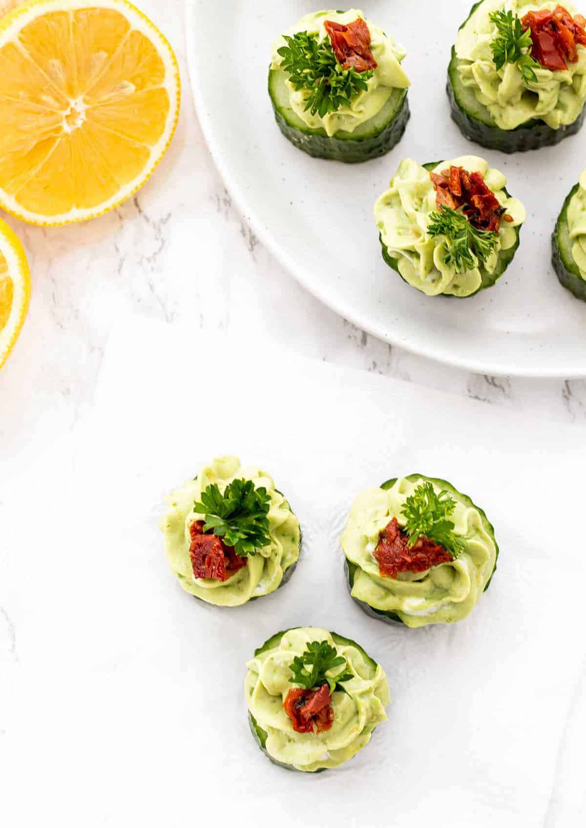 A plate of cucumber rounds topped with green avocado mousse and garnished with sundried tomatoes and parsley.