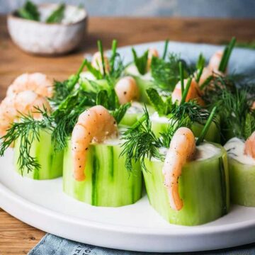 Plate of cucumber rolls filled with yoghurt and dill, topped with shrimp and garnished with additional dill.