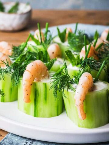 Plate of cucumber rolls filled with yoghurt and dill, topped with shrimp and garnished with additional dill.