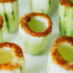 Cucumber cups with spiced rims on a white surface.
