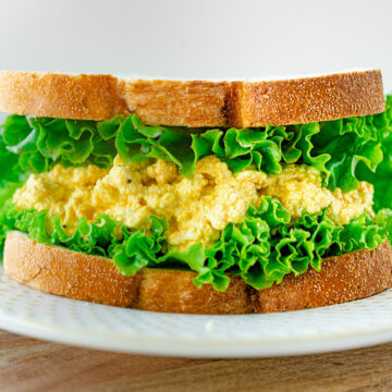 A vegan egg salad sandwich with frilly lettuce on a plate.