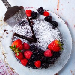 A round chocolate cake dusted with powdered sugar, topped with strawberries, raspberries, and blackberries.