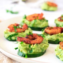 Cucumber Shrimp Bite appetizers topped with mashed avocado and seasoned shrimp are arranged on a white plate.