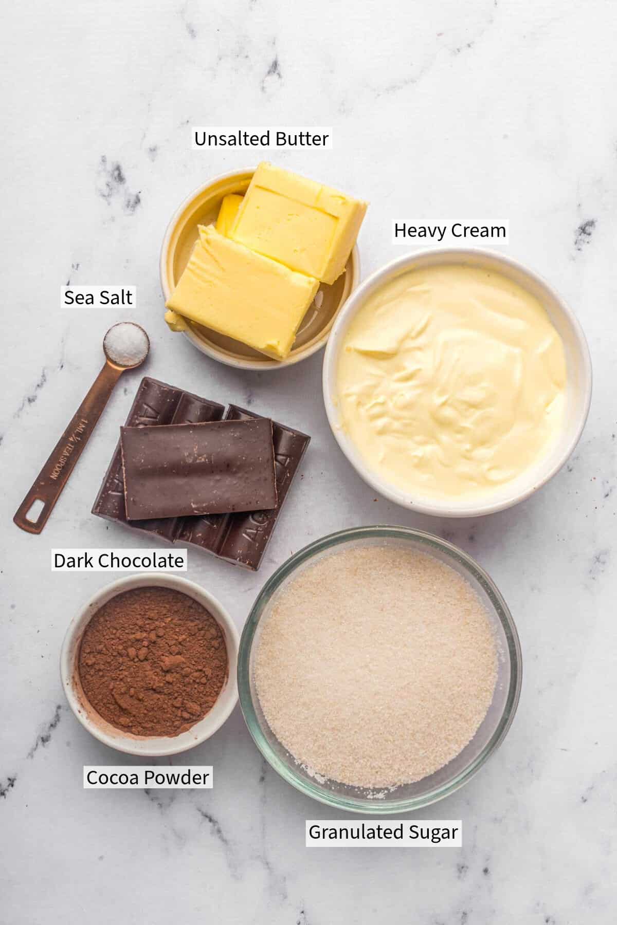labelled ingredients for chocolate fudge frosting placed on a marble countertop.