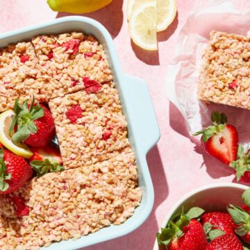 A baking dish of strawberry rice krispie treats with a piece cut out, garnished with fresh strawberries and lemon slices.