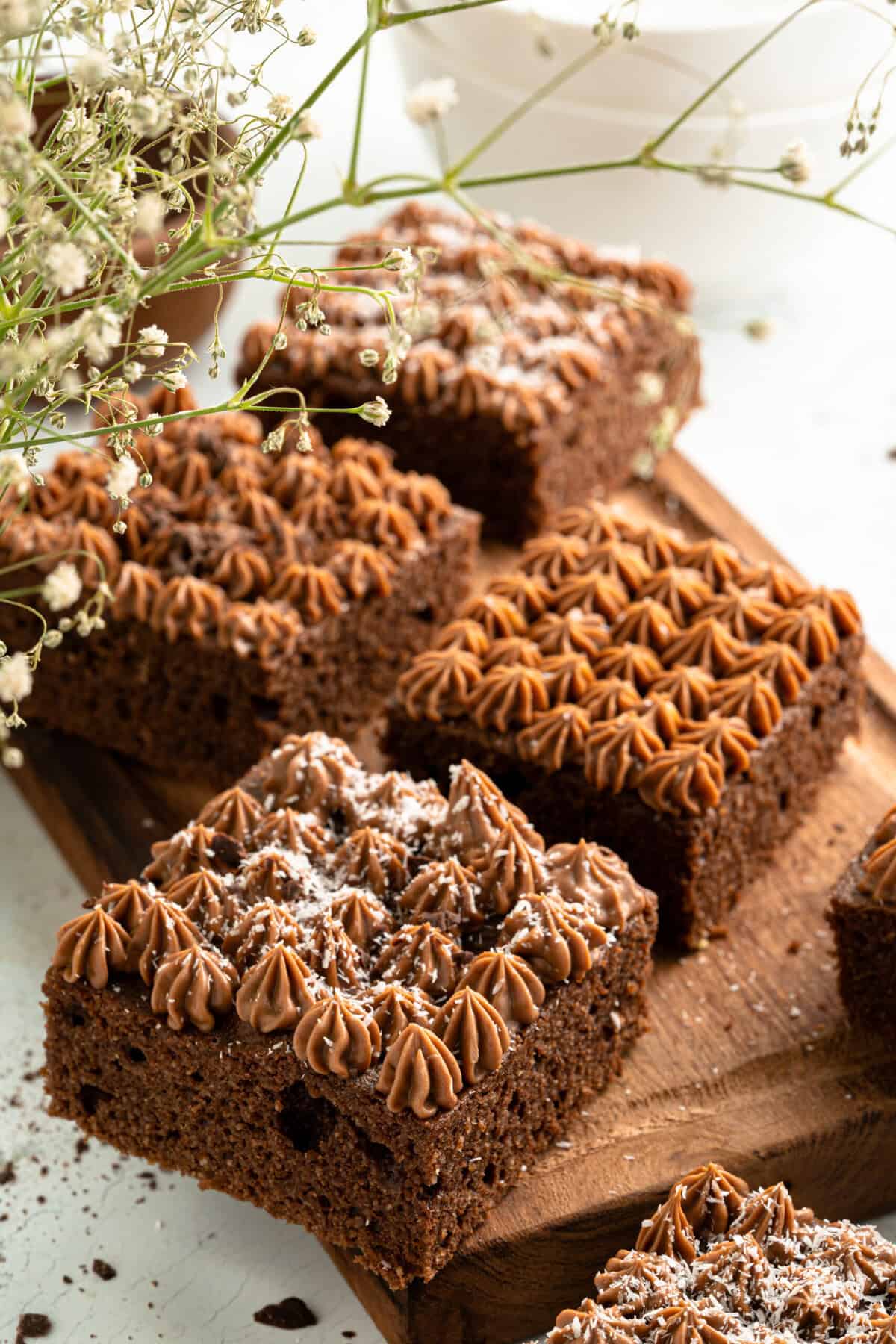 A close-up of sugar-free chocolate cake squares topped with piped chocolate frosting sitting on a wooden board. 