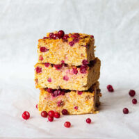 Three apple cake slices with visible red berries are stacked on a white, crumpled paper background.