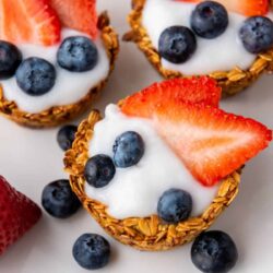 Granola cups filled with yogurt and topped with fresh blueberries and strawberry slices.