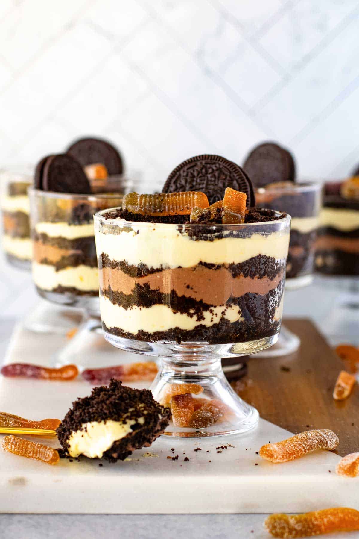 Four layered Oreo dirt cake cups topped with cookies and gummy worms, displayed on a marble surface.