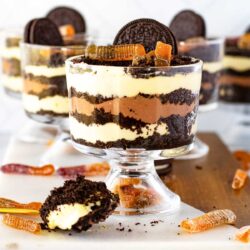 Glass bowls filled with layered Oreo Dirt Cakes with gummy worms. A spoonful of the dessert is placed in the foreground.