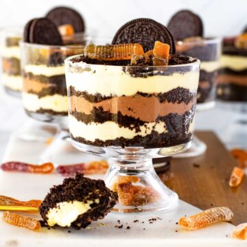 Glass bowls filled with layered Oreo Dirt Cakes with gummy worms. A spoonful of the dessert is placed in the foreground.