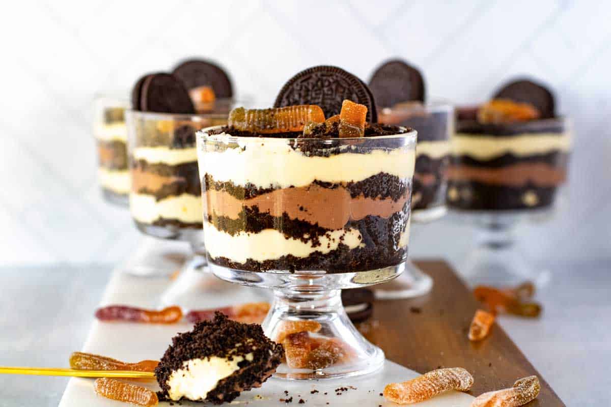 Four layered Oreo dirt cake cups topped with cookies and gummy worms, displayed on a marble surface.