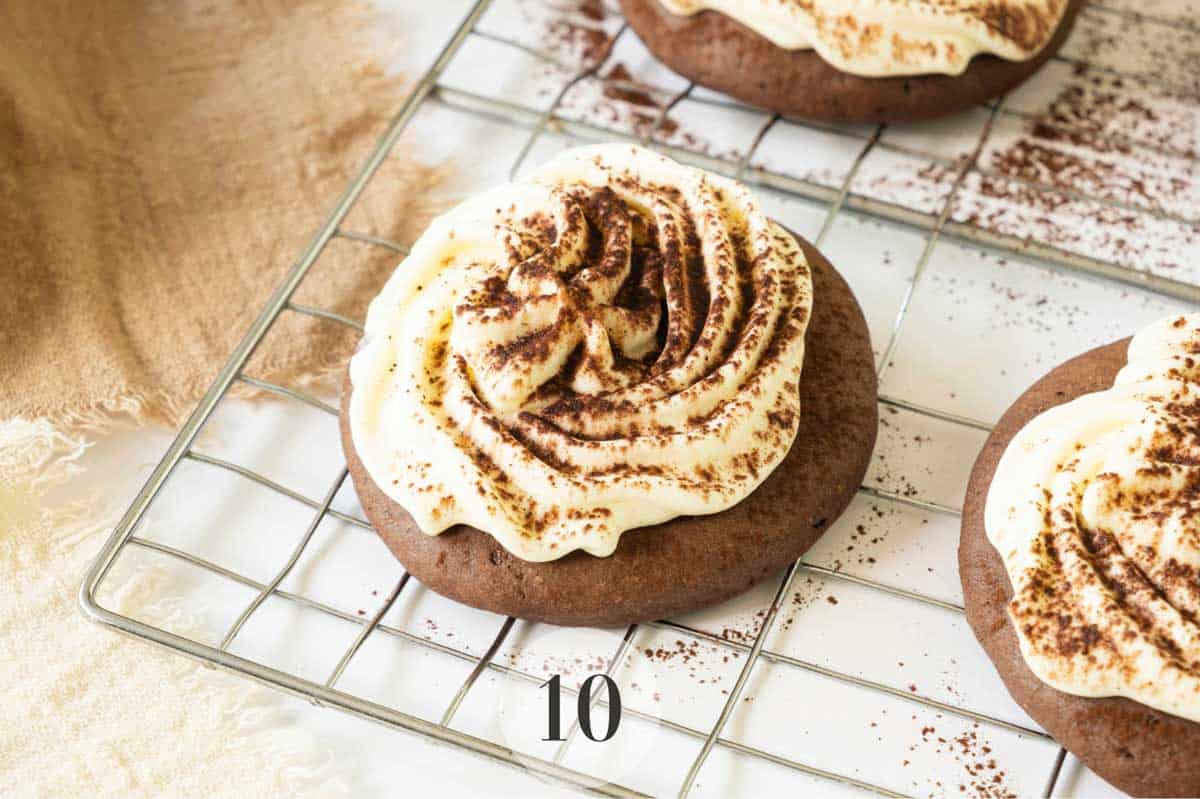 Tiramisu Cookies with swirls of cream and sprinkled cocoa powder on a cooling rack, numbered "10".