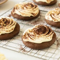 Tiramisu Cookies with white frosting and cocoa powder on top, placed on a cooling rack.