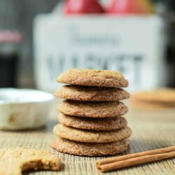 A stack of six cinnamon sugar cookies on a mat, with one partially eaten cookie in the foreground and a small bowl and market box in the blurred background.