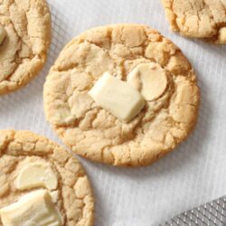 A close-up of baked cookies with pieces of white chocolate on a cooling rack lined with parchment paper.